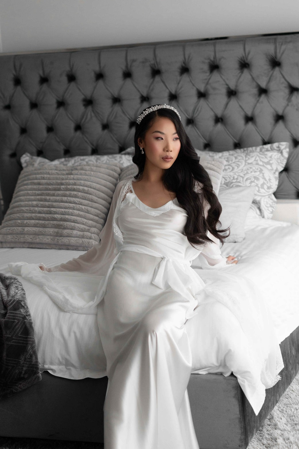 Bride wearing lace trim bridal robe with bridal tiara on bed