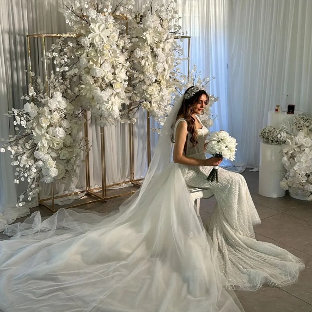 Bride in a silver bridal headpiece white wedding dress sitting in front of a floral archway.