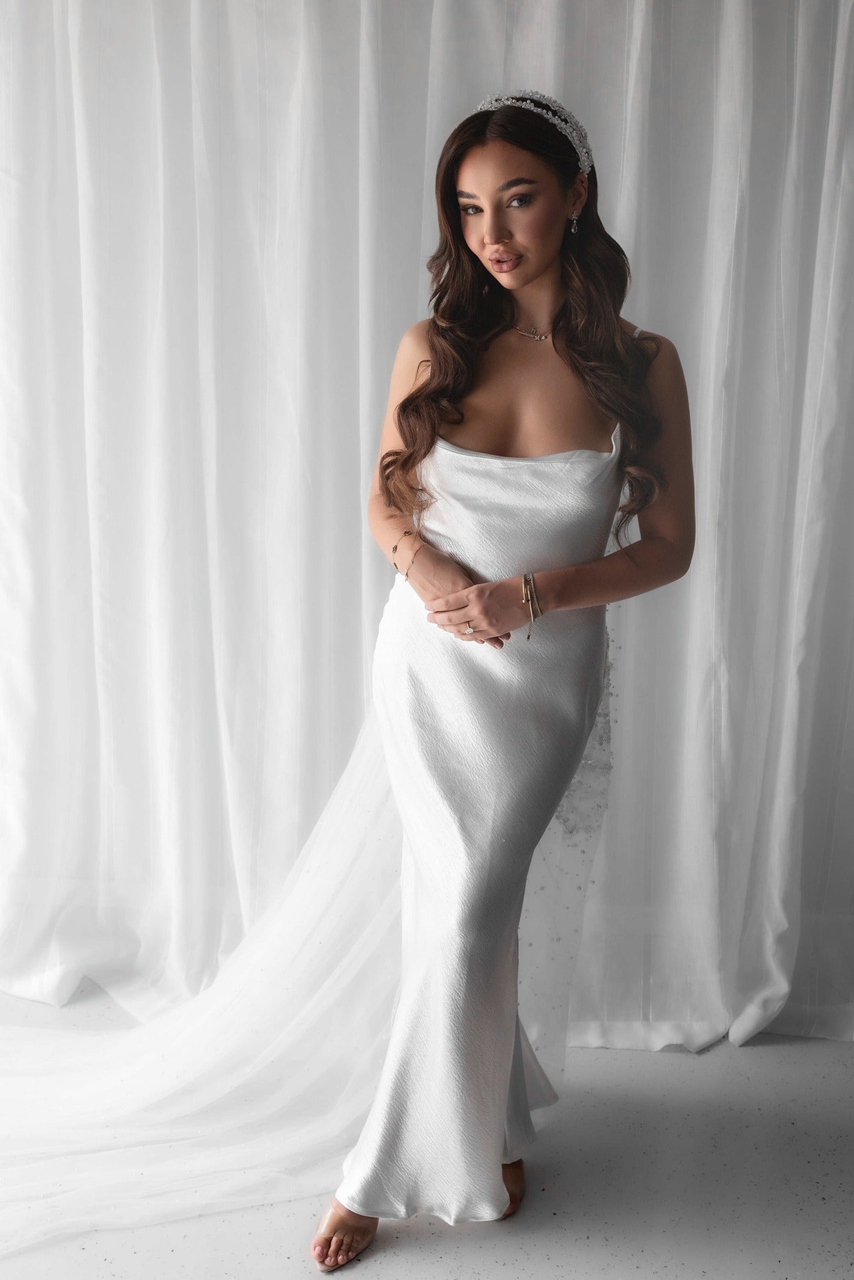 Woman in a white bridal slip dress standing against a white curtain