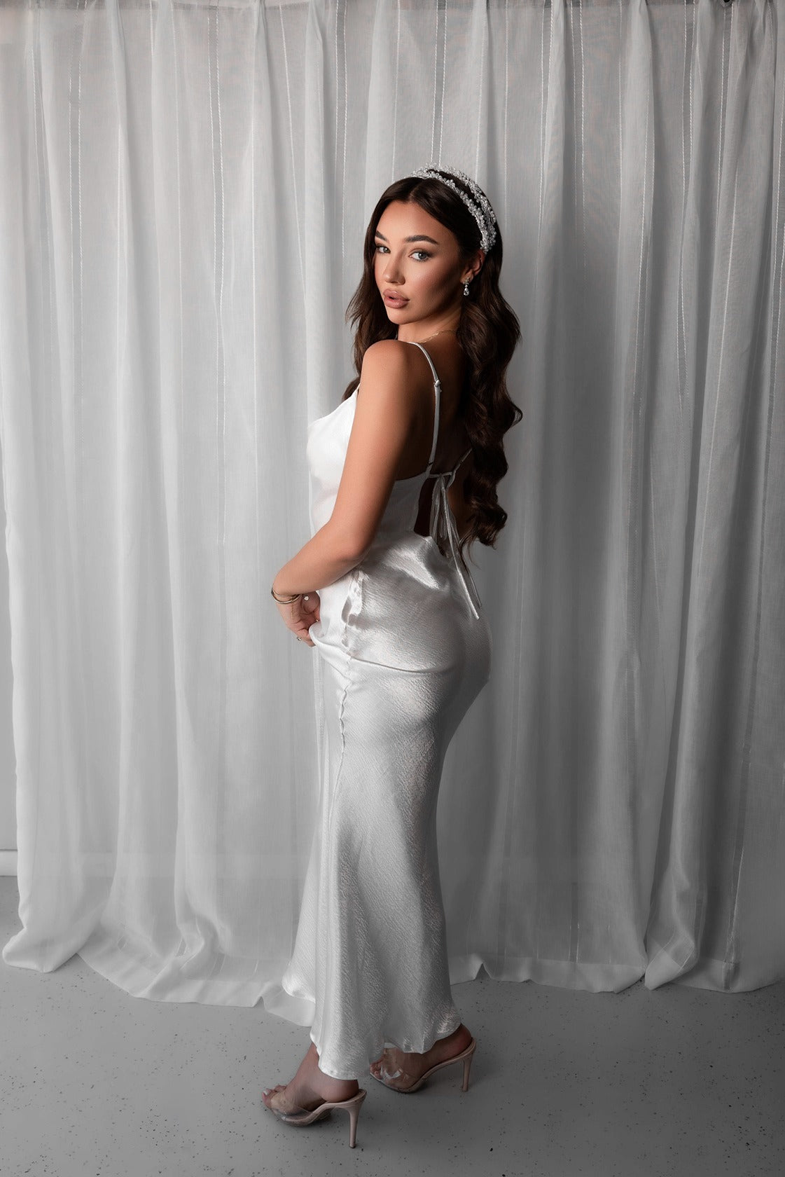 Woman in a white bridal slip dress standing against a white curtain