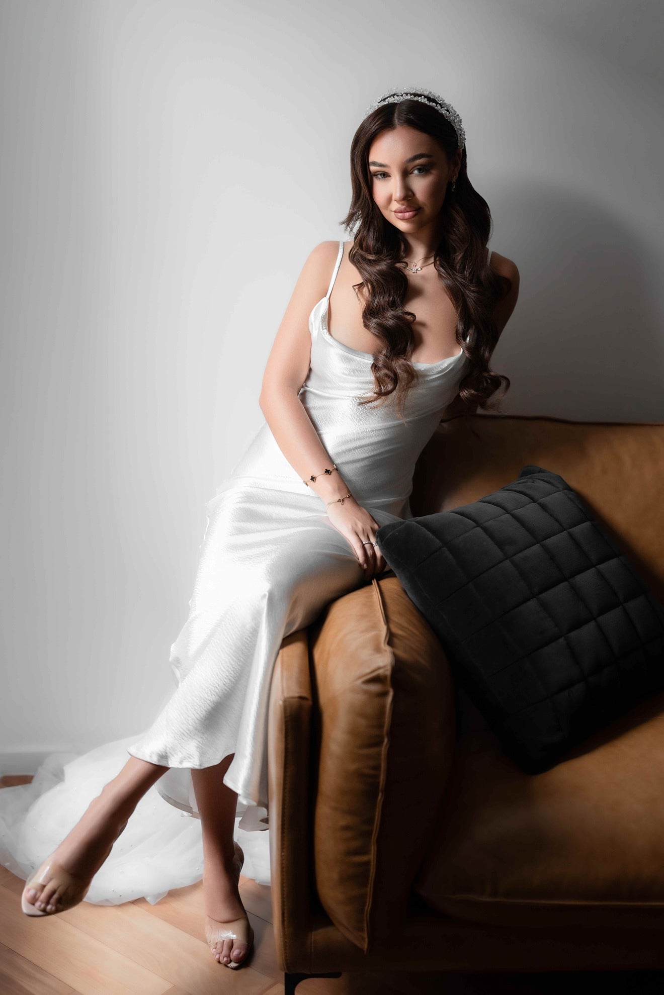 Woman in a white bridal slip dress sitting on a brown couch with a gray pillow.