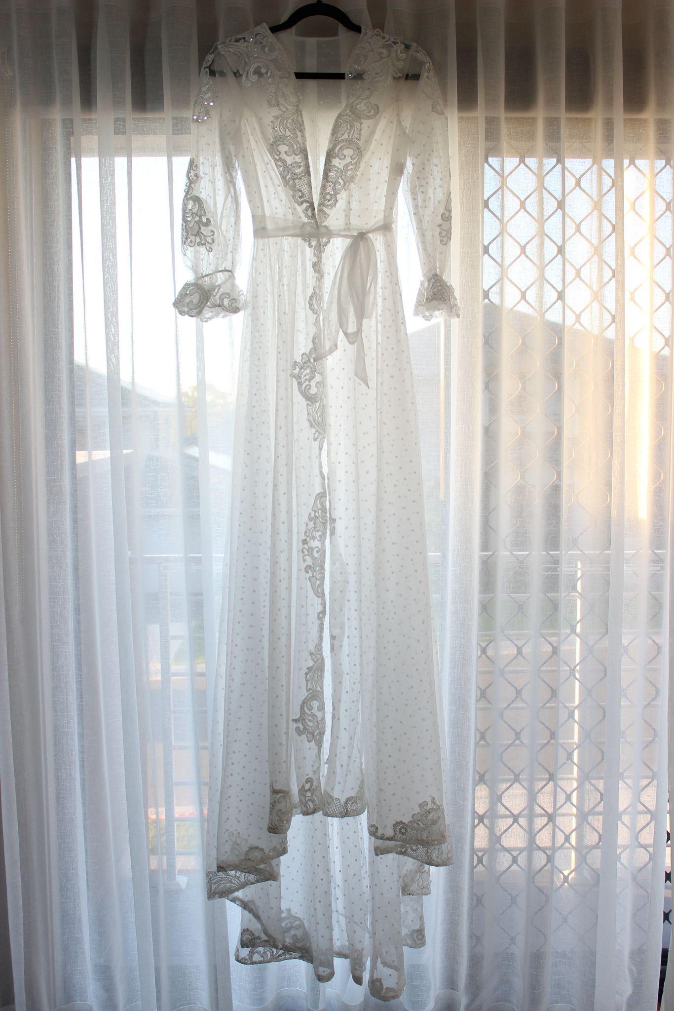 Ariana Lace Robe hanging on a black hanger against a white curtain background