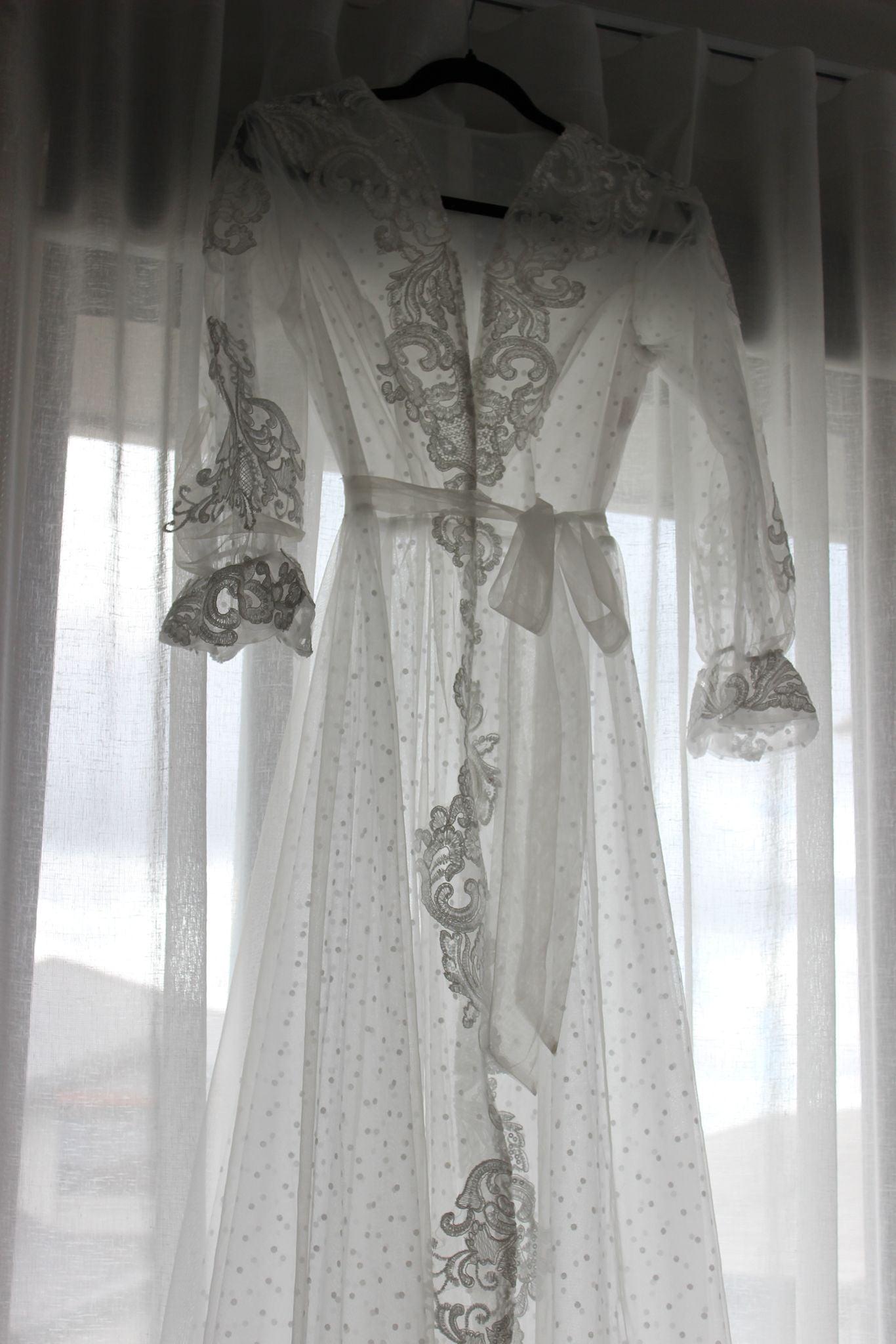 Close-up of the Ariana Lace Robe hanging on a black hanger against a white curtain