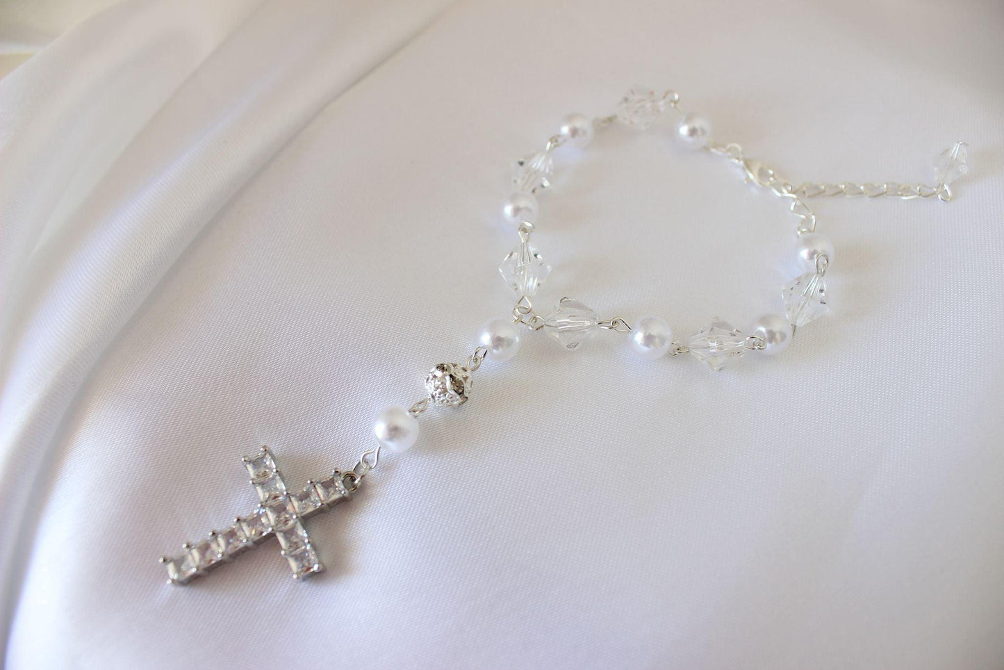 Wedding rosary bracelet with crystals, pearls, and large cross displayed on white cloth