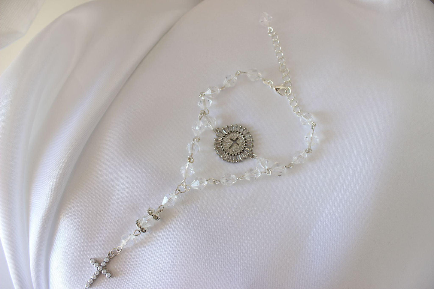Bridal rosary bracelet with drop chain and cross emblem displayed on white cloth