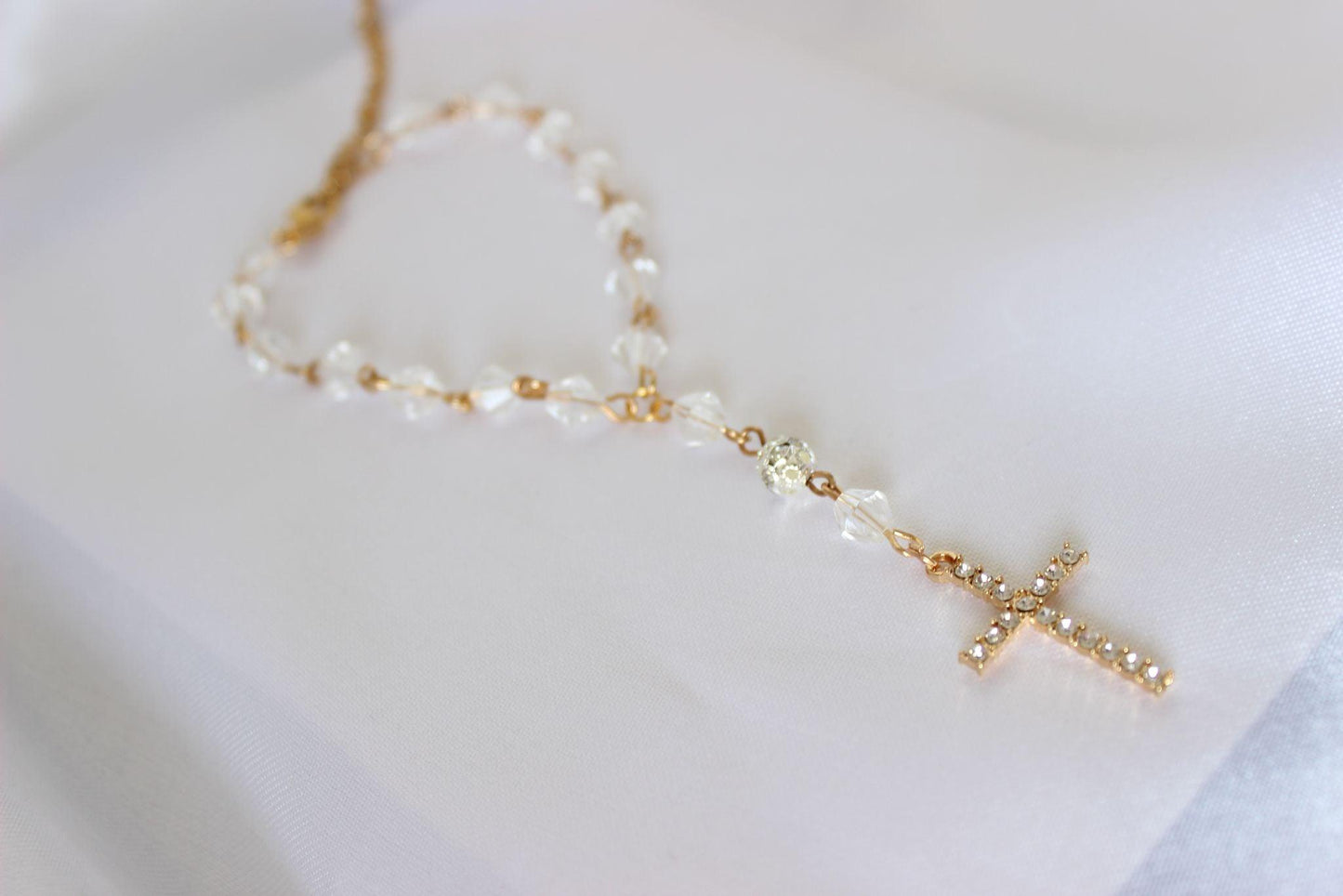 bridal rosary bracelet with a gold cross and crystal beads displayed on white cloth