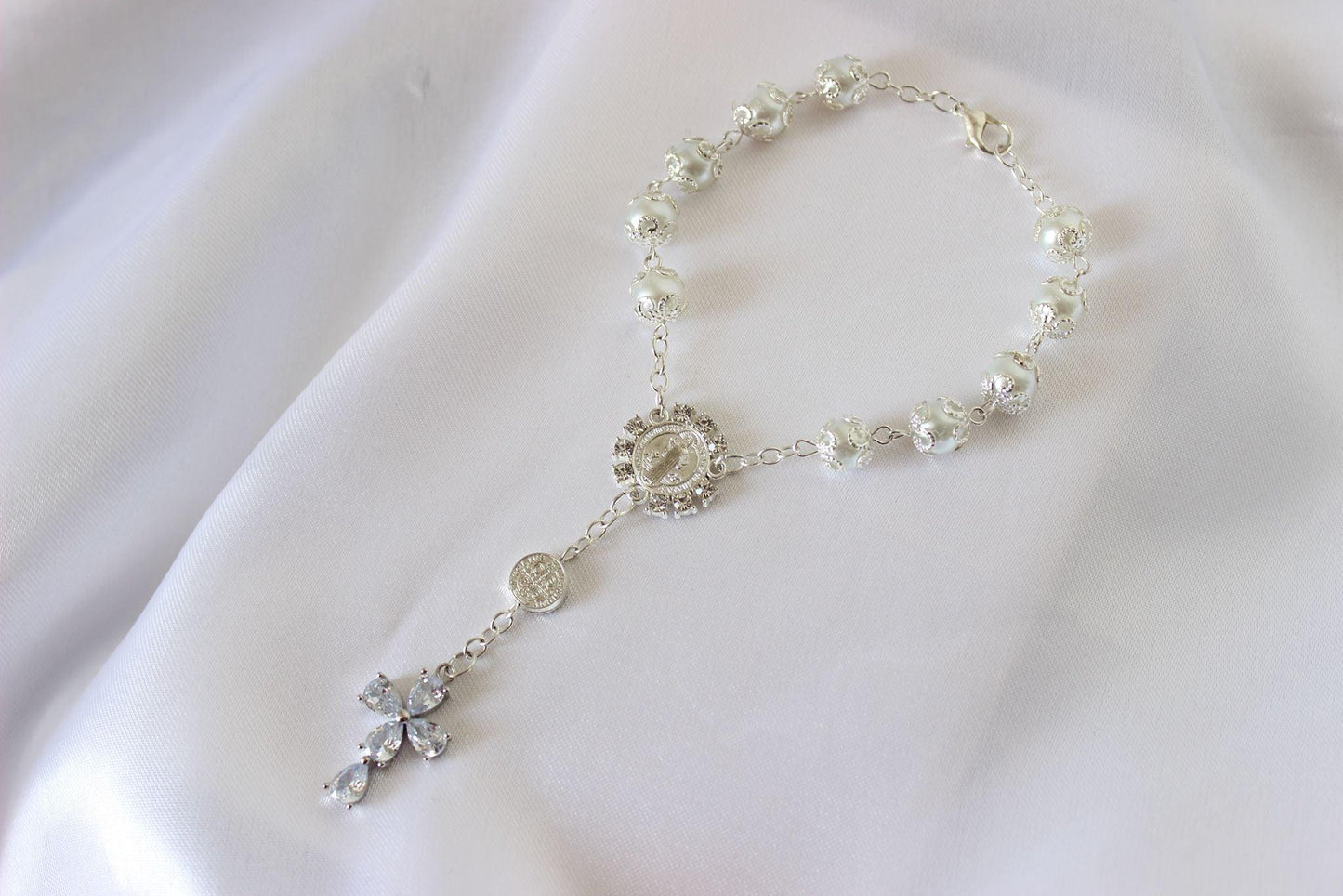 Bridal rosary bracelet with marquise cross displayed on white cloth background