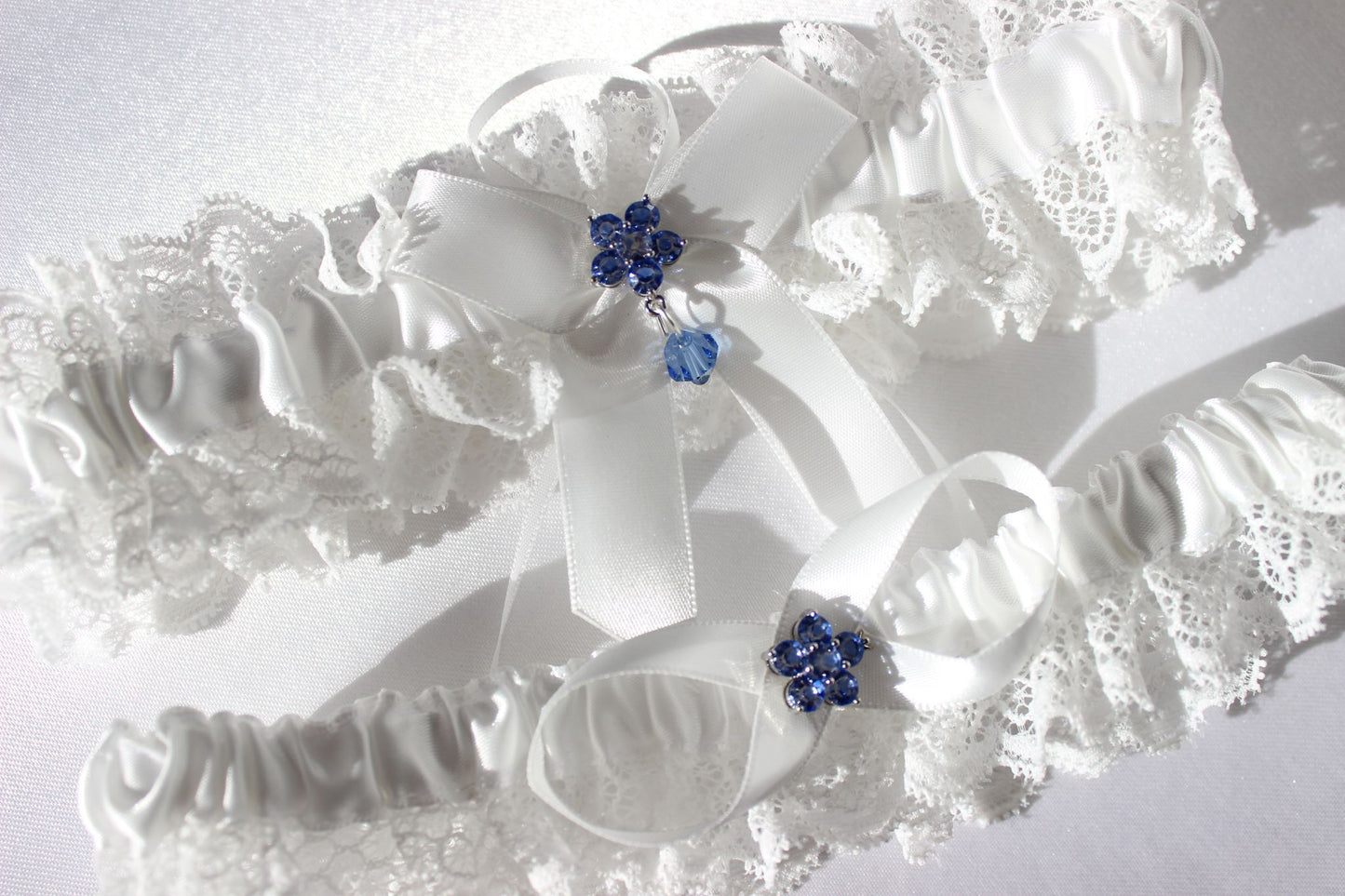 Close up of white lace bridal garter with central blue flower on white background