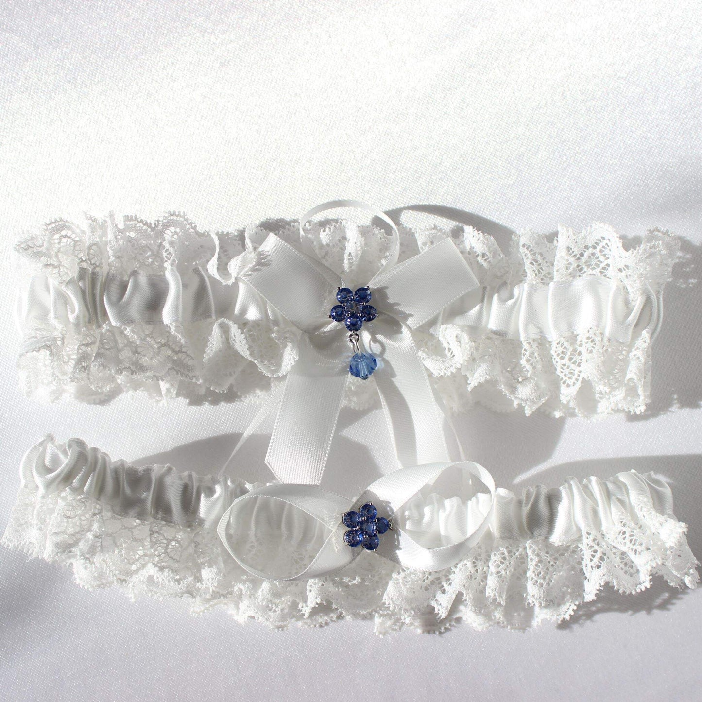 White bridal garter set with lace and central blue flower emblems on white background