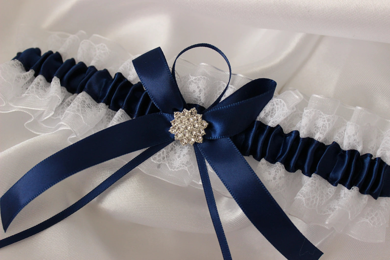 Navy blue and white lace bridal garter on white satin background