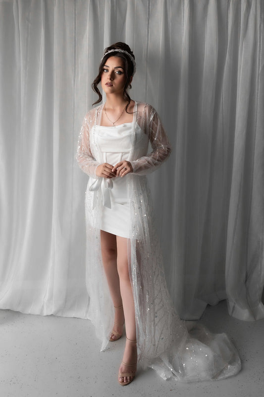 Woman in a bridal slip dress with a bridal robe standing against a white curtain.