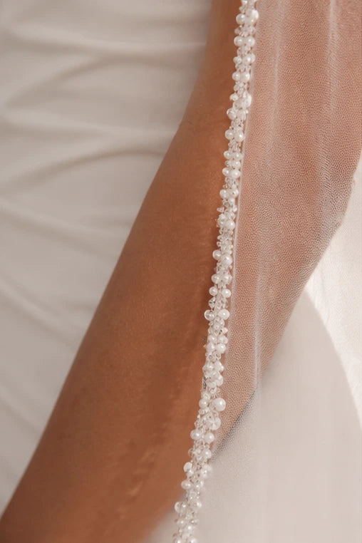 A close-up of a pearl bridal veil draped over a person's arm, decorated with a vertical line of small white pearls.
