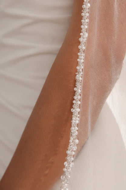 A close-up of a pearl bridal veil draped over a person's arm, decorated with a vertical line of small white pearls.