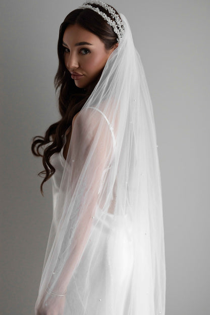 Woman wearing a white wedding pearl veil and bridal headband against a gray background