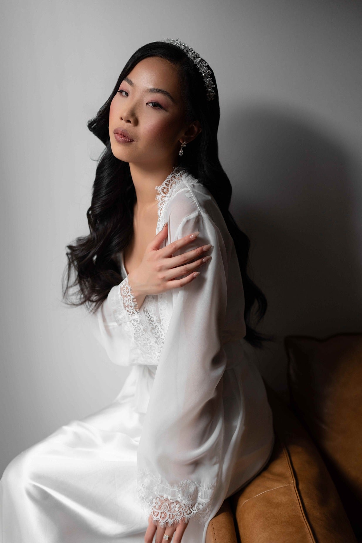 Woman in a white bridal robe sitting on a brown couch against a gray wall.