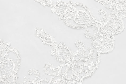 White floral lace trim with intricate embroidered patterns and scalloped edges, shown in a close-up detail view.