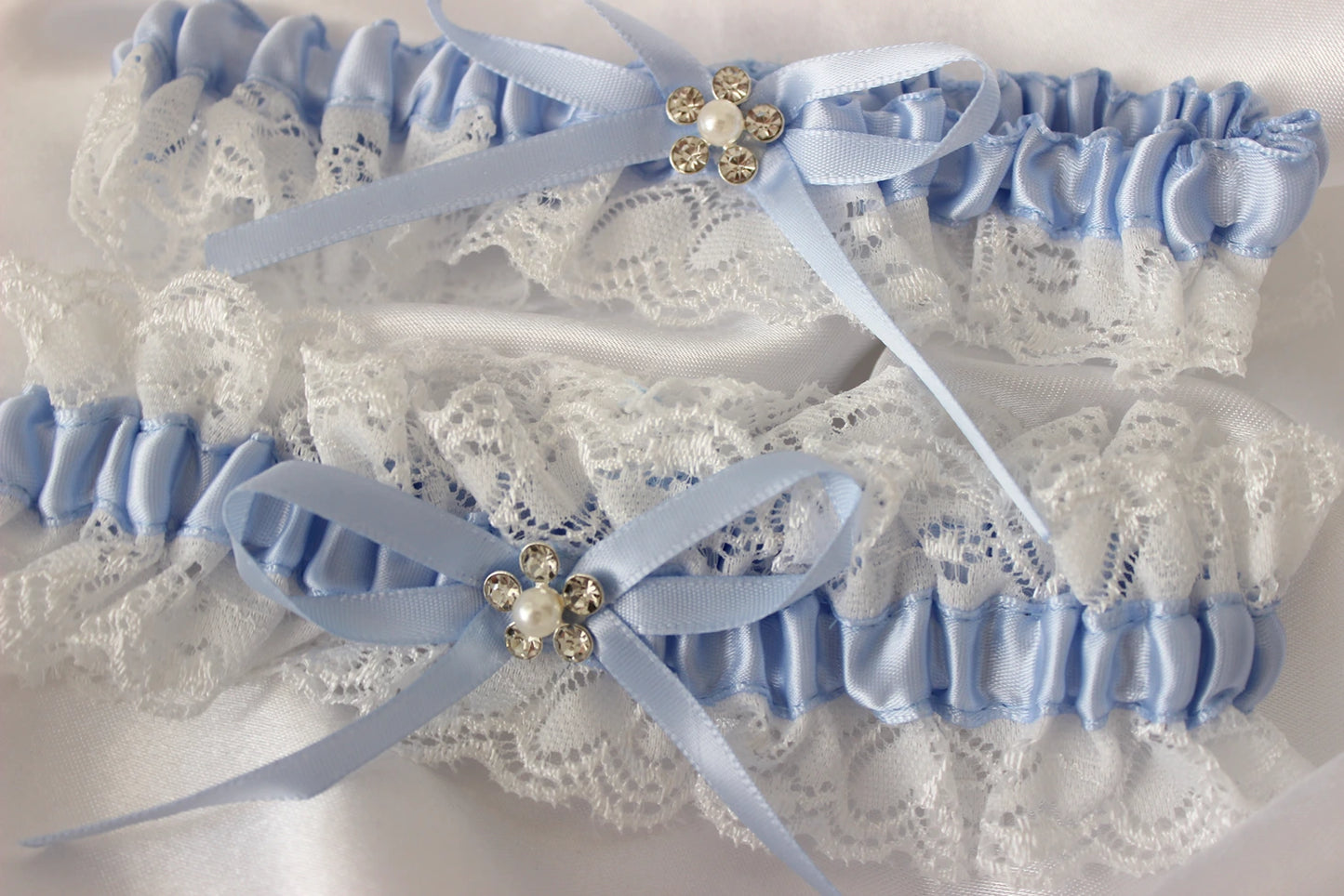 Pair of light blue garters with lace detailing and decorative ribbons on a white background
