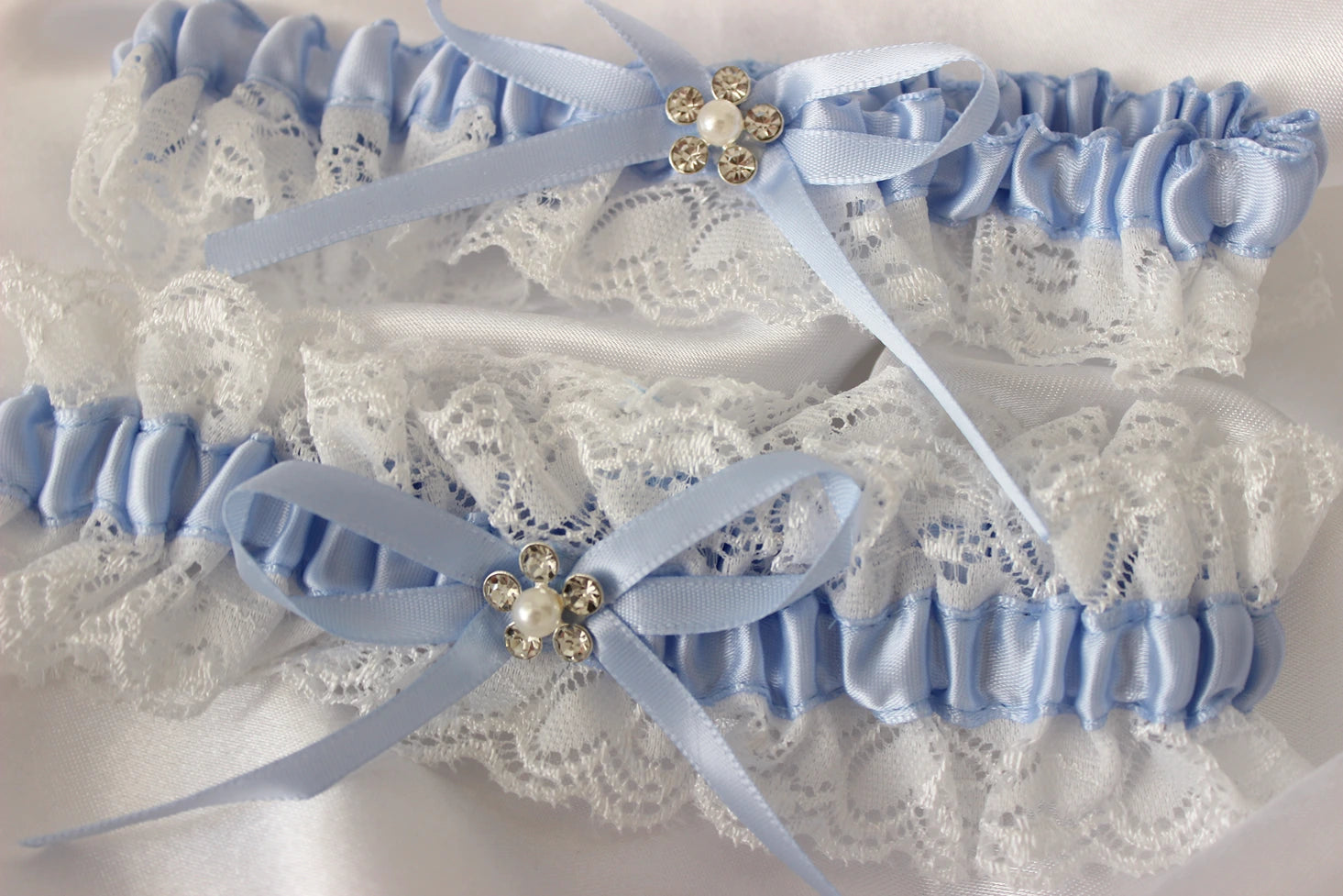 Pair of light blue garters with lace detailing and decorative ribbons on a white background