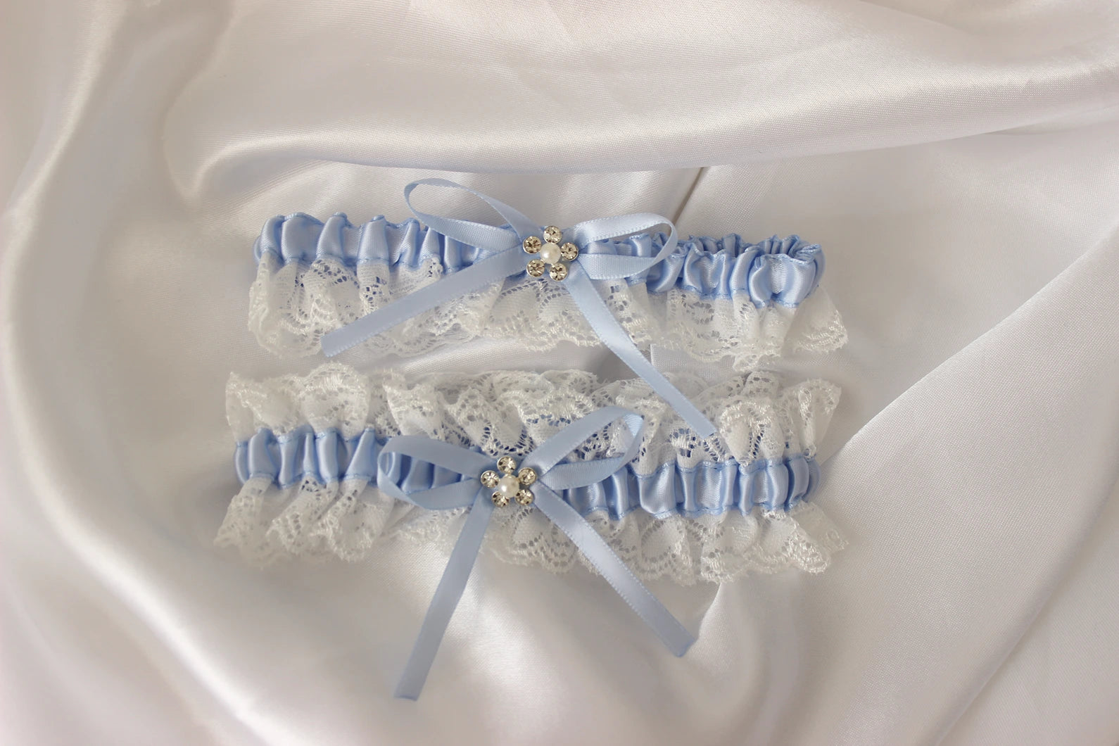 Pair of light blue lace garters with decorative ribbons on a white fabric background