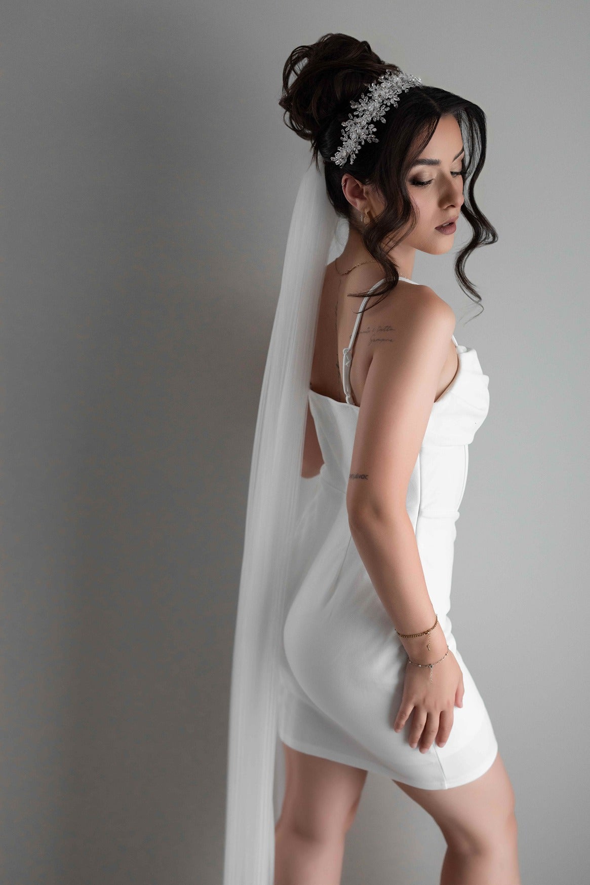 Woman in a white bridal slip dress with a veil against a gray background