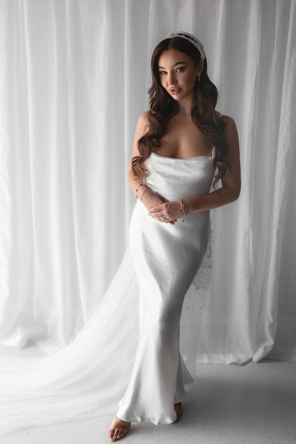 Woman in a white bridal slip dress standing against a white curtain
