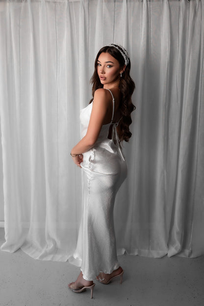 Woman in a white bridal slip dress standing against a white curtain