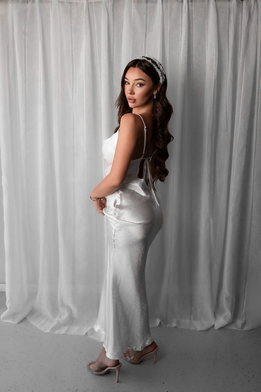 Woman in a white bridal slip dress standing against a white curtain