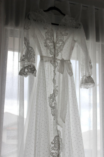 Close-up of the Ariana Lace Robe hanging on a black hanger against a white curtain