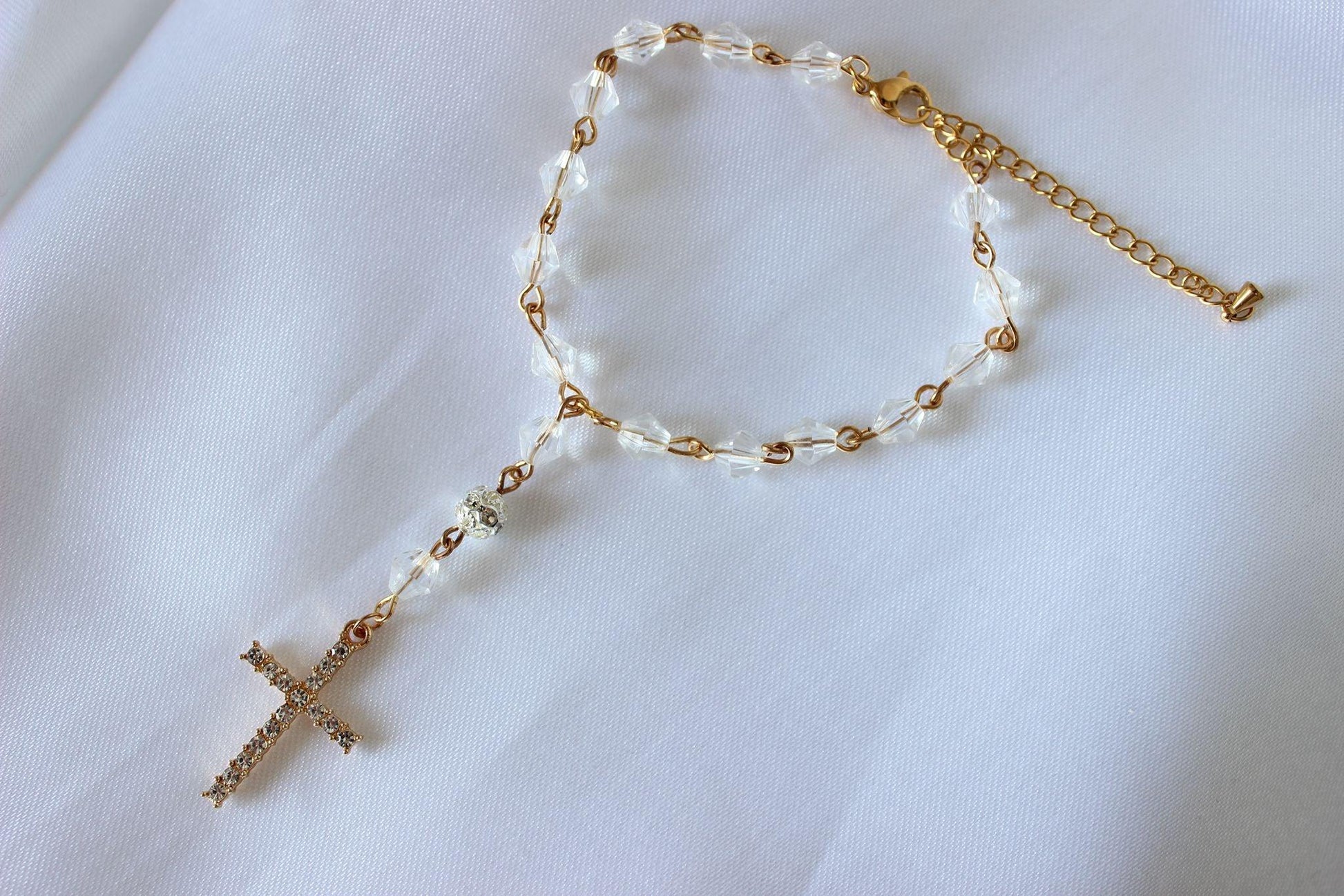 Bridal rosary bracelet with gold cross and crystal beads displayed on white cloth