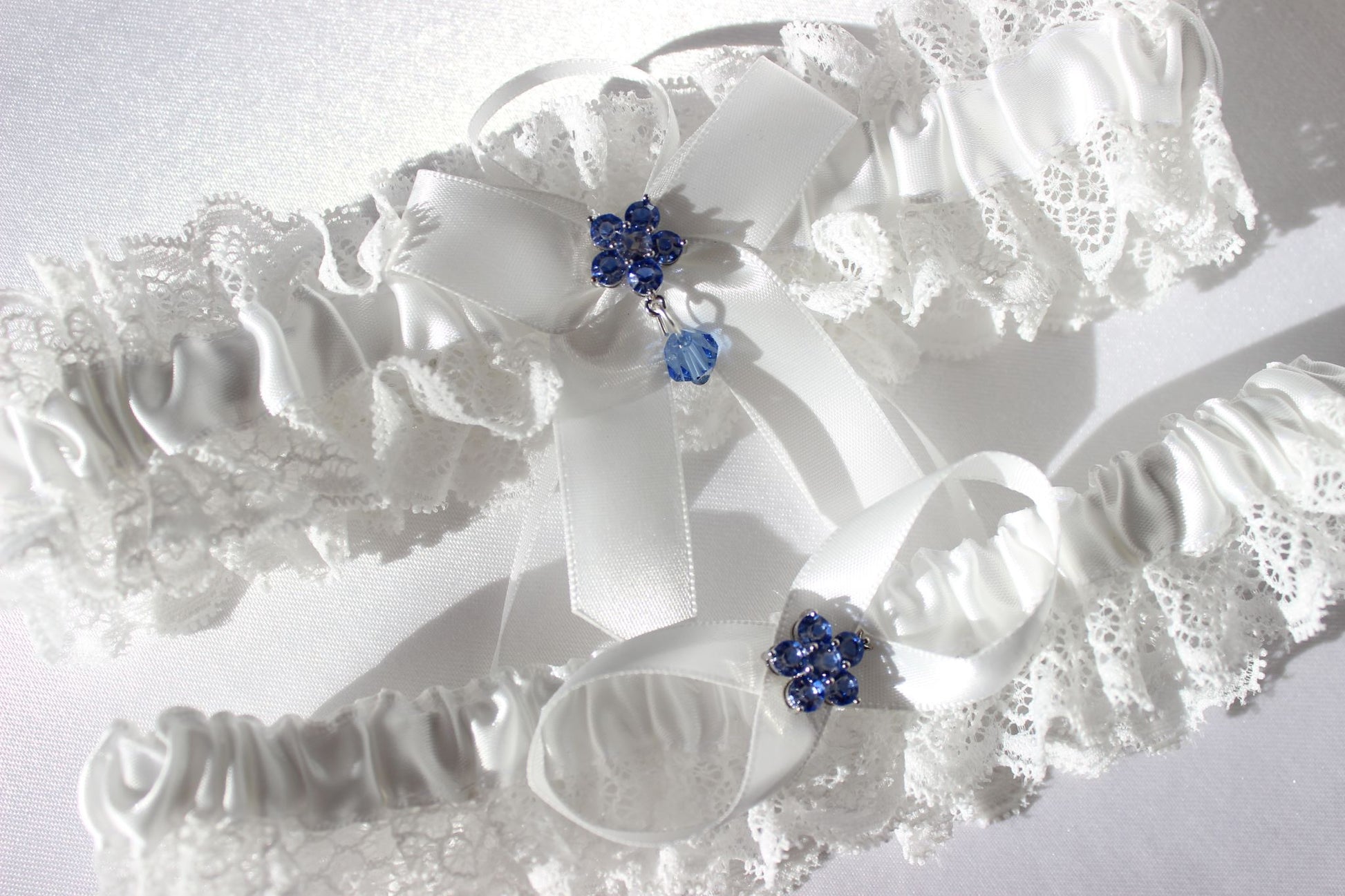 Close up of white lace bridal garter with central blue flower on white background