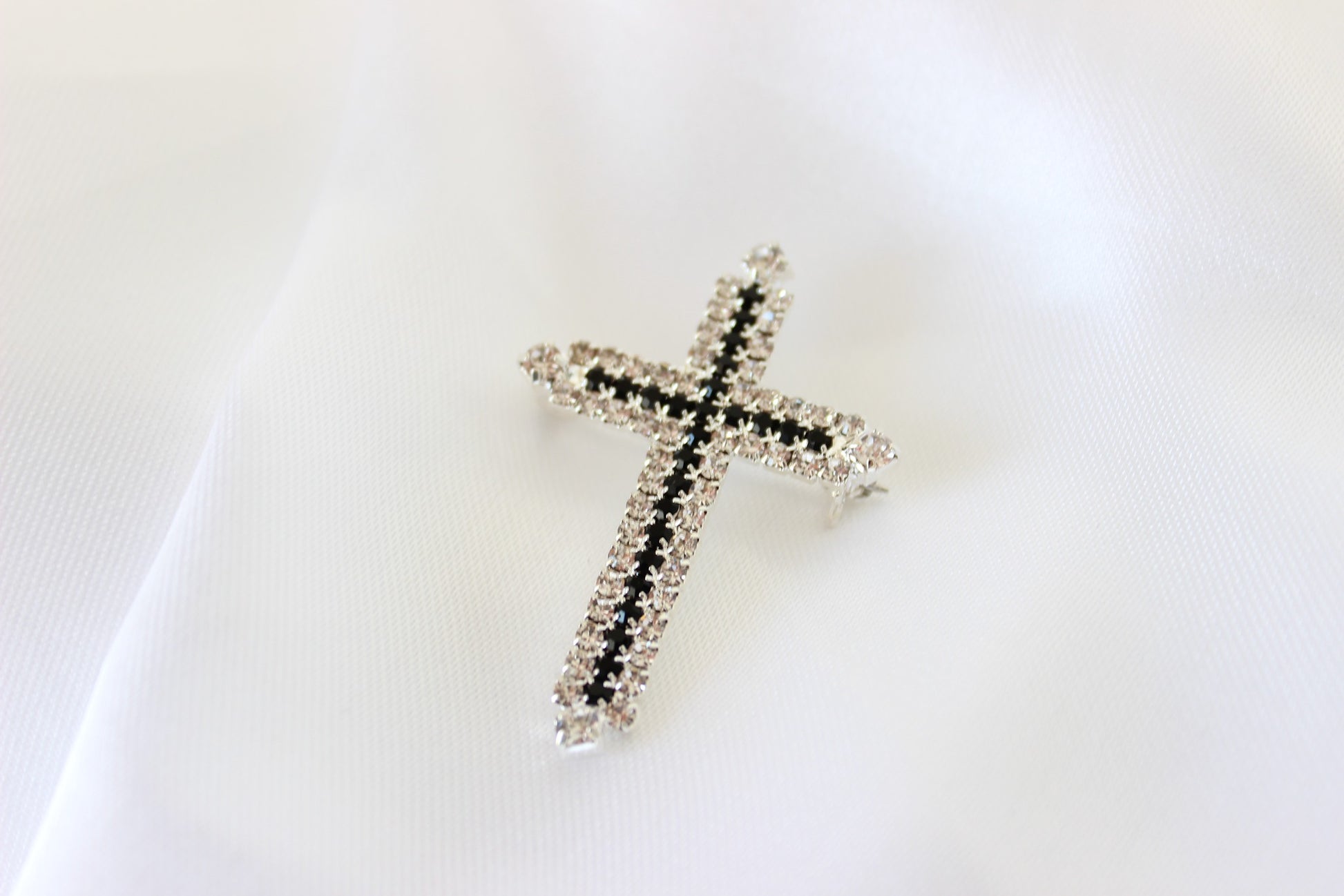 Silver and black cross brooch on white background